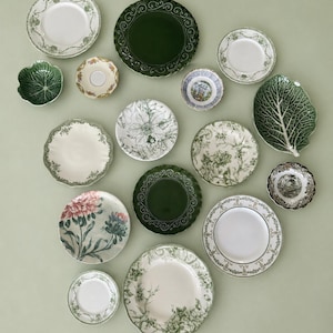 May include: A collection of various ceramic plates and bowls featuring diverse designs, including solid dark green scalloped edges, intricate floral patterns in green and white, a cabbage leaf-shaped dish, and detailed botanical illustrations.