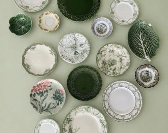 May include: A collection of various ceramic plates and bowls featuring diverse designs, including solid dark green scalloped edges, intricate floral patterns in green and white, a cabbage leaf-shaped dish, and detailed botanical illustrations.