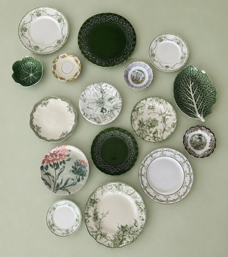 May include: A collection of various ceramic plates and bowls featuring diverse designs, including solid dark green scalloped edges, intricate floral patterns in green and white, a cabbage leaf-shaped dish, and detailed botanical illustrations.