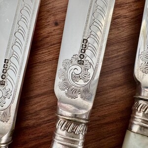 Pu&ograve; includere: Primo piano di tre coltelli da tavola in argento con disegni decorativi e punzoni. I coltelli hanno un manico in argento e una lama con un motivo decorativo.