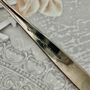 Może przedstawiać: Srebrzysty uchwyt sztućca ze stali nierdzewnej z wygrawerowanym napisem Community oraz słowem STAINLESS. Metalowa powierzchnia jest gładka i odblaskowa, ukazując wyraźny odcisk nazwy marki wykonany pismem kursywnym.