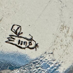 May include: Close-up of a silver-colored surface with a small, stylized bee illustration. The bee is black and has a simple, cartoonish design. The surface has a textured appearance.