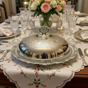 Pu&ograve; includere: Una tavola da pranzo apparecchiata per un pasto formale. Un piatto da portata d'argento con coperchio ornato &egrave; su un piatto decorativo. Bicchieri di cristallo, posate e composizioni floreali completano l'elegante allestimento. La tovaglia ha un motivo floreale.