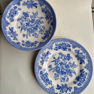 K&ouml;nnte beinhalten: Zwei blaue und wei&szlig;e Keramikteller mit einem Blumenmuster und einem Vogeldesign. Die Teller befinden sich auf einer wei&szlig;en Oberfl&auml;che.