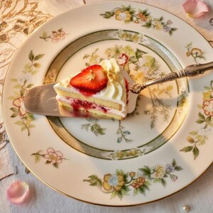 K&ouml;nnte beinhalten: Eine wei&szlig;e Keramik-Tasse mit schwarzem Henkel und dem Text "But First, Coffee" in fetter, schwarzer Schrift. Die Tasse steht vor einem verschwommenen Hintergrund, der eine gem&uuml;tliche Umgebung suggeriert.