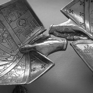 K&ouml;nnte beinhalten: Eine silberfarbene Skulptur, die zwei H&auml;nde zeigt, die Spielkarten halten. Die Karten sind aufgef&auml;chert und zeigen detaillierte Illustrationen von K&ouml;nigen, Damen und anderen Kartensymbolen. Die Skulptur hat eine detaillierte, strukturierte Oberfl&auml;che.