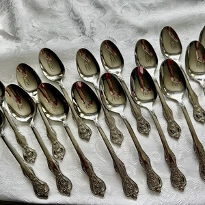 May include: A collection of silver spoons arranged on a white, patterned tablecloth. The spoons have a reflective surface and ornate, detailed handles. The spoons are likely for serving or dining.