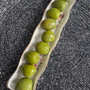 May include: A white ceramic dish with a floral design holds a row of green olives.