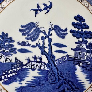 May include: Blue and white porcelain plate with a traditional willow pattern design. The pattern features a bridge, a willow tree, a pagoda, and two birds in flight.