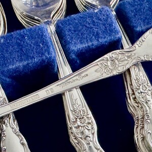 K&ouml;nnte beinhalten: Ein Satz silberner L&ouml;ffel mit verzierten Blumenmustern. Die L&ouml;ffel sind auf der R&uuml;ckseite mit "Victorian Rose" und "U.S. A. " graviert.