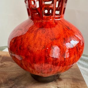 Puede incluir: Un jarr&oacute;n de cer&aacute;mica brillante en tonos rojos y naranjas. El jarr&oacute;n tiene un cuerpo bulboso y un cuello cil&iacute;ndrico con un dise&ntilde;o geom&eacute;trico recortado. La base es de color marr&oacute;n oscuro.