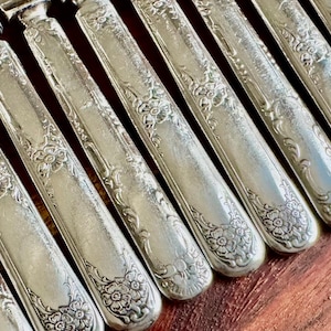 May include: A set of eight silver-plated dinner knives with ornate floral designs on the handles.