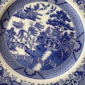 K&ouml;nnte beinhalten: Blau-wei&szlig;e Keramikplatte mit einem traditionellen chinesischen Weidenmuster. Das Design zeigt eine Pagode, eine Br&uuml;cke, einen Weidenbaum und einen Fluss.