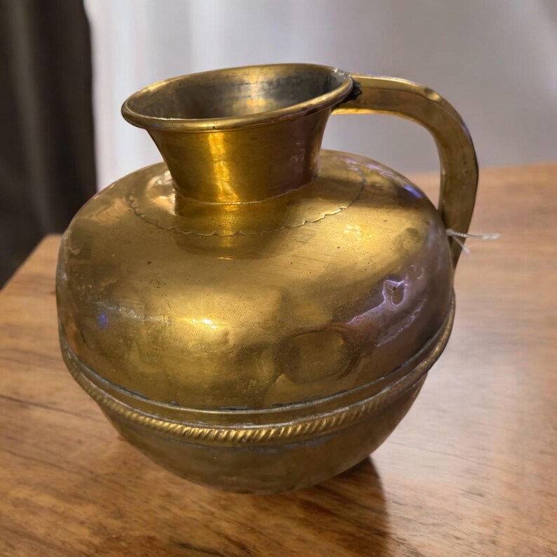 K&ouml;nnte beinhalten: Eine kleine, runde Kanne aus Messing mit einem Henkel. Die Kanne hat einen dekorativen Band um die Mitte.