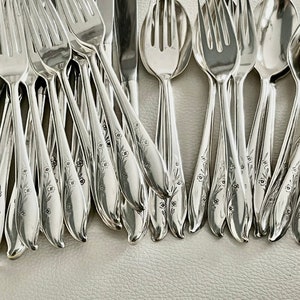 May include: A collection of shiny silver flatware, including forks, spoons, and knives. Each piece is adorned with a delicate floral pattern along the handle. The silverware is arranged on a light-colored surface.