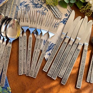 May include: A stainless steel cutlery set comprising four spoons, four forks and five knives. Each piece features a textured, ornate handle with a repeating geometric pattern. The set is arranged on a wooden surface, showcasing the polished metal finish and the detailed, embossed design on the handles of the utensils.