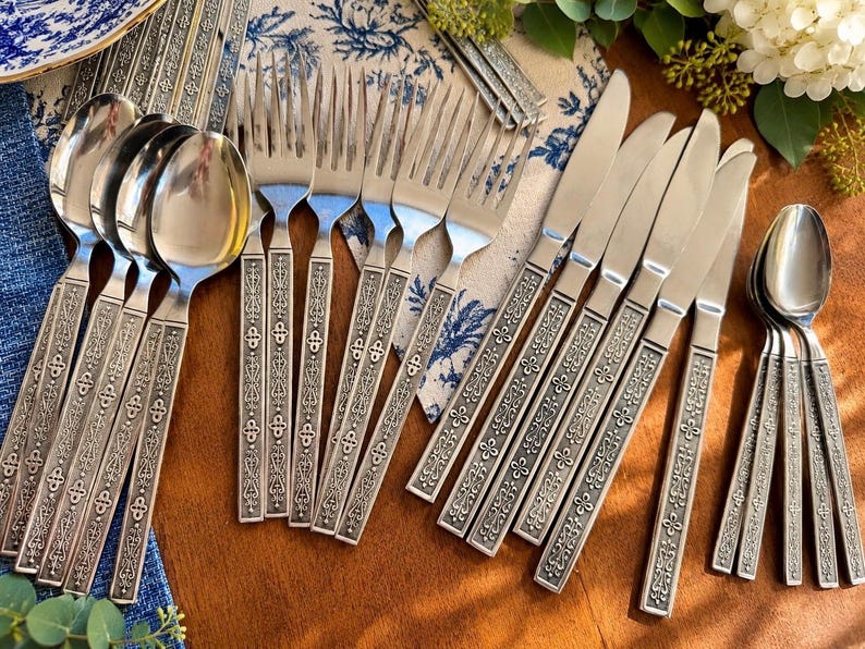 May include: A stainless steel cutlery set comprising four spoons, four forks and five knives. Each piece features a textured, ornate handle with a repeating geometric pattern. The set is arranged on a wooden surface, showcasing the polished metal finish and the detailed, embossed design on the handles of the utensils.