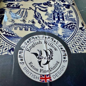 K&ouml;nnte beinhalten: Eine blau-wei&szlig;e English Willow-Platte mit einer detaillierten Landschaftsszene. Die Platte zeigt eine Br&uuml;cke, Figuren und eine Pagode. Ein Aufkleber mit dem Text "English Willow British Design" ist sichtbar.