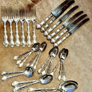 May include: A set of silverware, including forks, knives, and spoons, with ornate handles. The silverware is arranged on a brown, fuzzy surface.