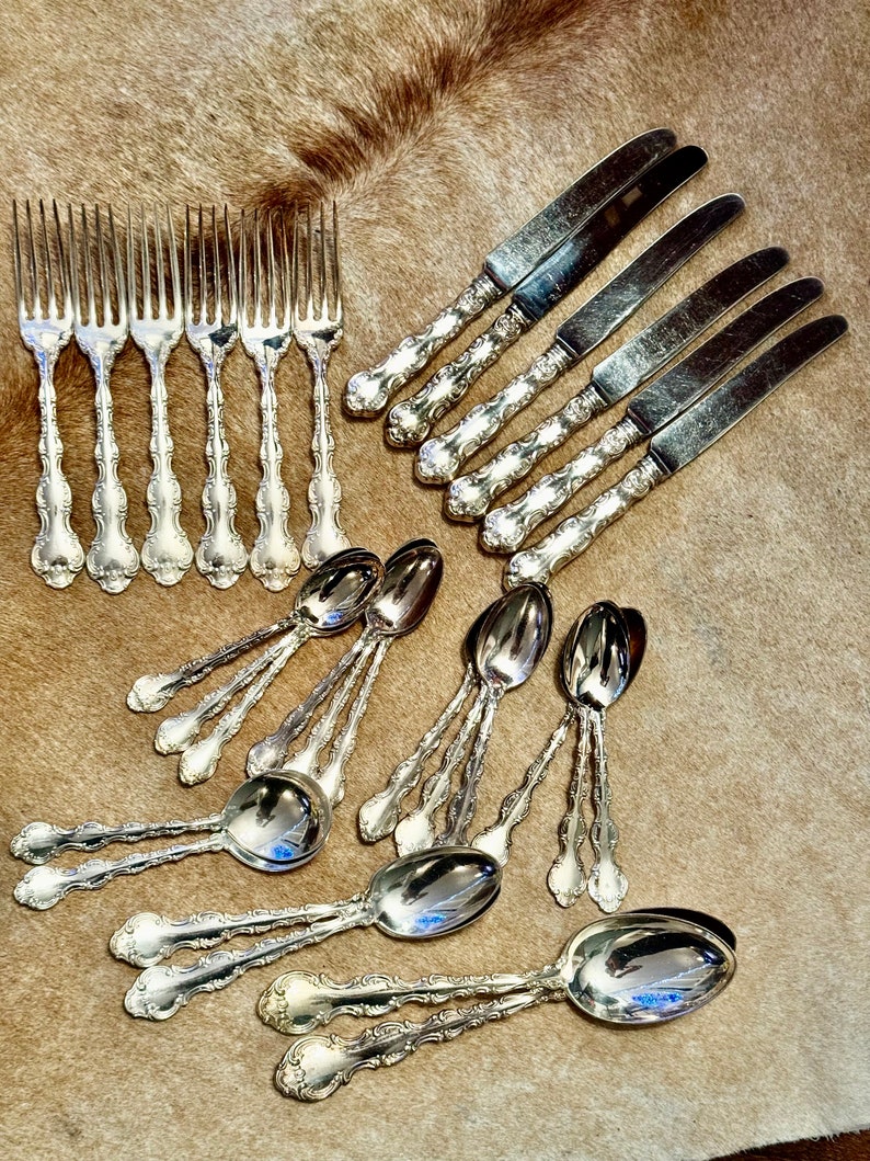 May include: A set of silverware, including forks, knives, and spoons, with ornate handles. The silverware is arranged on a brown, fuzzy surface.