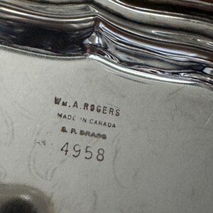 May include: A silver-toned metal tray with a scalloped edge. The surface features the stamped text: WM. A. ROGERS, MADE IN CANADA, S. P. BRASS, and the number 4958. The metal has a reflective finish with subtle surface scratches.