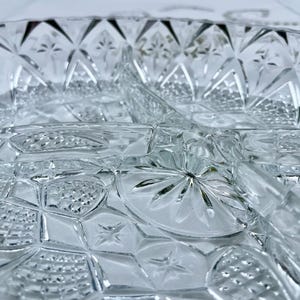 May include: Close-up of a clear, divided glass serving dish. The dish features a detailed, geometric pattern with star and diamond shapes. The glass has a textured surface, reflecting light.