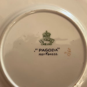 K&ouml;nnte beinhalten: Ein wei&szlig;er Keramikteller mit einem gr&uuml;n-goldenen Logo, auf dem "Ainsley England" und "Pagoda" mit der Nummer "K94635" steht.