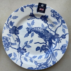 May include: A white ceramic plate featuring a blue transferware pattern of a long-tailed bird perched on flowering branches. A black tag at the top displays the text Royal Wessex, Made in England, and Est. 1795 with a small Union Jack flag icon.