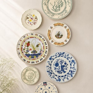 Op de afbeelding: Een verzameling van zeven ronde keramische borden gerangschikt in een groep. De borden hebben diverse ontwerpen, waaronder bloemmotieven, landschapssc&egrave;nes en blauw-witte patronen. Sommige borden hebben geschulpte randen, andere zijn glad.