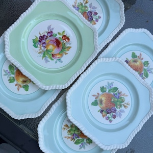 Puede incluir: Un juego de cinco platos de ensalada vintage con fondo blanco y borde verde o azul. Cada plato presenta un dise&ntilde;o de frutas coloridas con una fruta central rodeada de uvas y bayas.