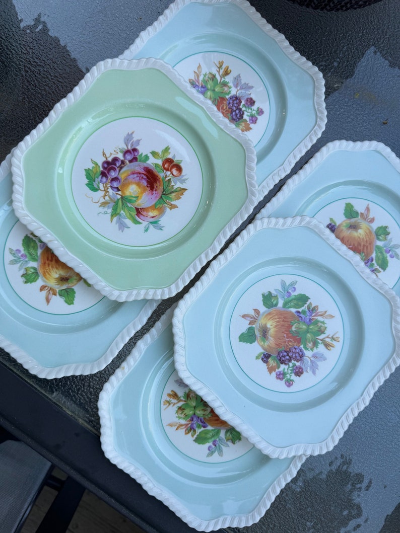 Puede incluir: Un juego de cinco platos de ensalada vintage con fondo blanco y borde verde o azul. Cada plato presenta un dise&ntilde;o de frutas coloridas con una fruta central rodeada de uvas y bayas.