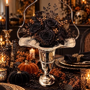 May include: A silver-toned metal basket with a tall arched handle, filled with a floral arrangement of dark black roses, small golden berries, and dark foliage. The basket features a wide, flared rim with a decorative perforated edge pattern.