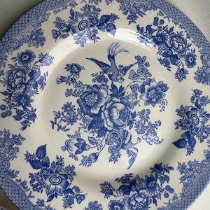 K&ouml;nnte beinhalten: Ein wei&szlig;er Keramik-Dinnerteller mit einem blauen und wei&szlig;en Blumenmuster. Das Muster zeigt einen Vogel und Blumen.