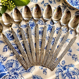 May include: A set of ten stainless steel spoons arranged in a fan pattern. Each spoon features a polished oval bowl and a long, slender handle decorated with an embossed floral and geometric pattern along the entire length of the stem.