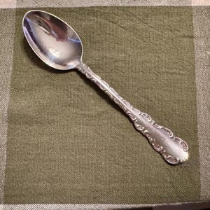 May include: A white ceramic mug with a black handle and the text "But First, Coffee" in a handwritten style. The mug is on a white surface. The mug is 10 cm tall.