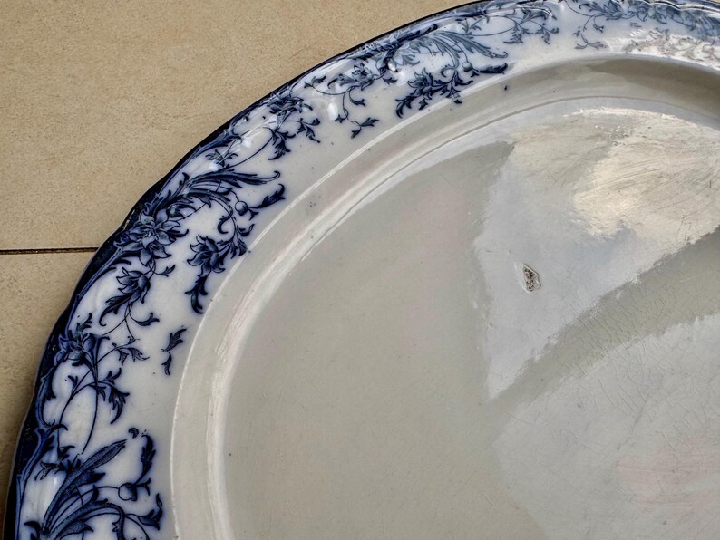 Puede incluir: Un plato de cer&aacute;mica blanca con un borde floral azul. El plato tiene un borde ligeramente curvado y un acabado brillante. El dise&ntilde;o floral azul es intrincado y detallado, agregando un toque de elegancia a la vajilla.