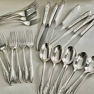May include: A collection of polished silver flatware, including forks, knives, and spoons. The silverware features a floral design on the handles. The arrangement includes multiple forks, knives, and spoons, suitable for a formal dining setting.