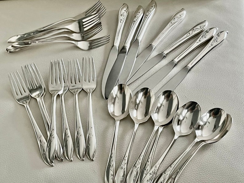 May include: A collection of polished silver flatware, including forks, knives, and spoons. The silverware features a floral design on the handles. The arrangement includes multiple forks, knives, and spoons, suitable for a formal dining setting.