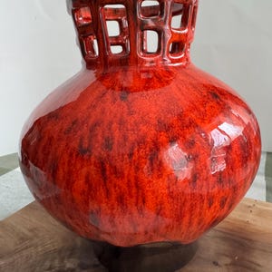 Puede incluir: Un jarr&oacute;n de cer&aacute;mica rojo grande con un acabado brillante. El jarr&oacute;n tiene un cuerpo bulboso y un borde calado marr&oacute;n oscuro. El esmalte rojo tiene motas oscuras y el jarr&oacute;n se asienta sobre una base marr&oacute;n oscuro. Un acento decorativo para el hogar.