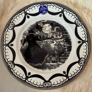 Może przedstawiać: Biały ceramiczny talerz obiadowy z czarno-białym wzorem halloweenowym. Talerz przedstawia czarnego kota, księżyc i dom ze straszną choinką. Talerz jest ozdobiony srebrem i ma logo "Royal Stafford" w środku.