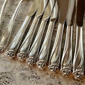 May include: A set of ten silver dinner knives with ornate floral designs on the handles.