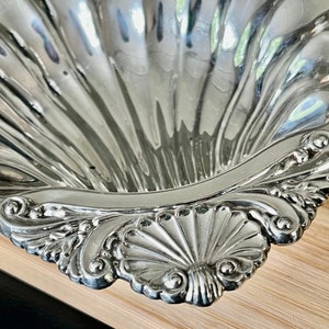 May include: A silver serving dish shaped like a seashell with intricate detailing around the rim.