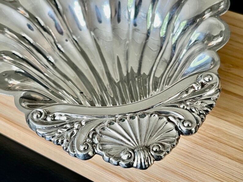 May include: A silver serving dish shaped like a seashell with intricate detailing around the rim.