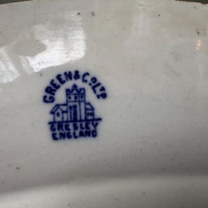 K&ouml;nnte beinhalten: Nahaufnahme einer blauen und wei&szlig;en Keramikmarke auf einem wei&szlig;en Teller. Die Marke lautet "Green & Co. Ltd. Gresley England".