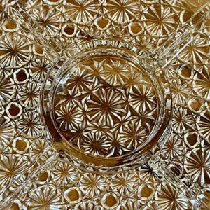 May include: Clear glass serving dish with a starburst pattern. The dish is divided into sections, with a central circular area and radiating compartments. The intricate design adds a touch of elegance to any table setting.