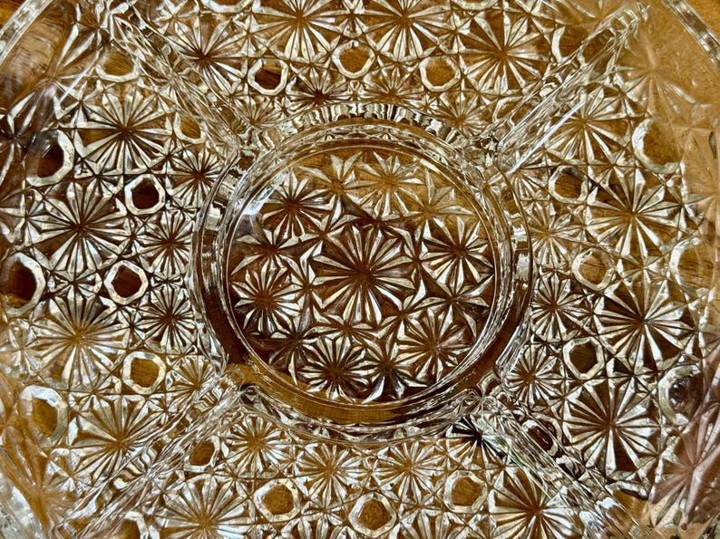 May include: Clear glass serving dish with a starburst pattern. The dish is divided into sections, with a central circular area and radiating compartments. The intricate design adds a touch of elegance to any table setting.