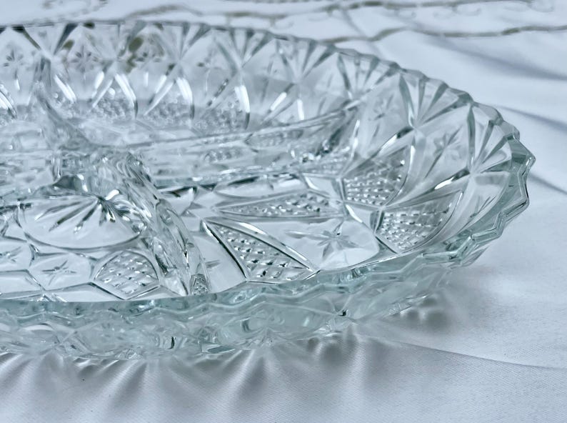 May include: Clear glass serving dish with three compartments. The dish has a diamond and starburst pattern. The rim has a scalloped edge. The dish is designed for serving appetizers or snacks.
