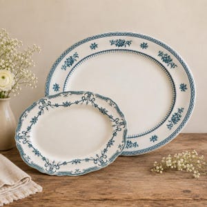 May include: Two oval ceramic platters featuring a cream-coloured base with a blue floral pattern along the scalloped edges. The larger platter has a simple border, while the smaller one displays an intricate garland design with ribbons.