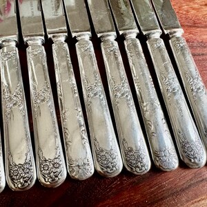 May include: A set of ten silver dinner knives with ornate floral designs on the handles.