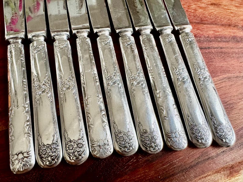 May include: A set of ten silver dinner knives with ornate floral designs on the handles.